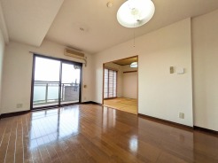 豊かな質感をたたえる床面が広がり、奥の和室とのつながりを感じさせる落ち着きのある空間